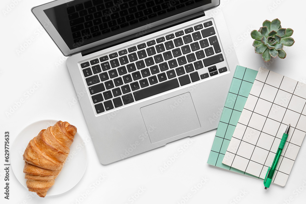Modern laptop, notebooks and croissant on white background