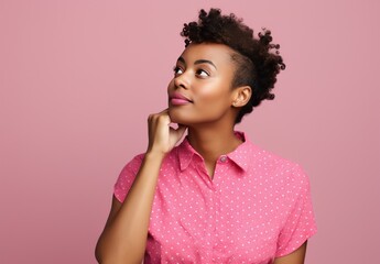 Portrait of a young woman in a pink shirt looking to the side and thinking, isolated on pink studio background.