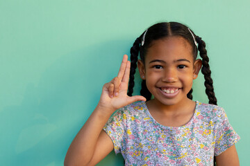 Biracial schoolgirl doing sign language gestures at elementary school, copy space