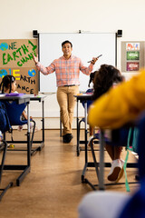 Wall Mural - Diverse happy male teacher with tablet and elementary schoolchildren sitting at desks in class