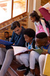 © WavebreakMediaMicro - Happy diverse male teacher and children with books sitting on stairs in class at elementary school