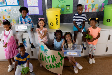 Portrait of happy diverse children with ecology items and plants in class at elementary school