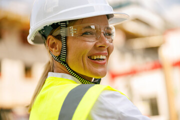 Smiling female construction worker in protective helmet standing against on construction background 