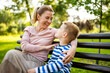 © djoronimo - Happy mother is sitting with her son on bench in park. They are having fun together.