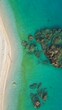 © iBu - Vista aérea de una costa rocosa y con arena clara. Aguas de mar cristalinas y en calma.