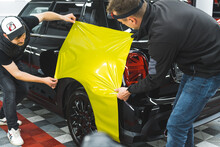 Skilled Professionals Using Special Lime Vinyl Film To Wrap A Black Car. Vehicle Wrapping Protecting The Paint. High Quality Photo