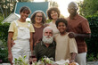 © pressmaster - Happy large intercultural family of three generations looking at camera with smiles while standing in front of served table during outdoor dinner