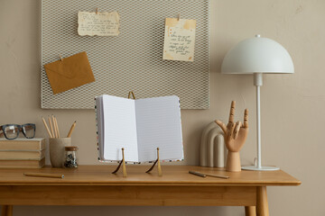 Creative composition of workplace interior with mock up poster frame, wooden desk, white lamp, stylish sculpture, beige wall and personal accessories. Home decor. Template.