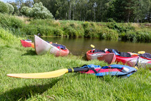 
Canoe With Yellow Paddle And Red Kayak On Grass.