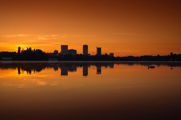 Wall Mural - Sunrise over Bucharest. Sunrise photo in the morning dusk with orange and blue sky with the skyline of Bucharest and reflection in Herastrau Lake. Travel to Romania.