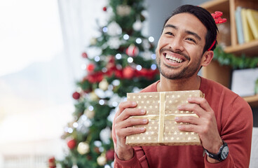 Canvas Print - Christmas, surprise and asian man with gift in his home happy, excited and having fun celebrating holiday. Hand holding, box and Japanese male with present in a living room at December party or event