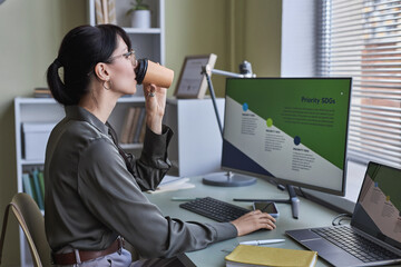 Wall Mural - Side view portrait of young woman drinking coffee in office while working on development strategies by deadline