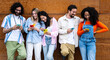 © carlesiturbe - Diverse young confident people smiling and using their phones outside in a city while leaning against a wooden wall. Multiracial group of friends texting on their smartphones