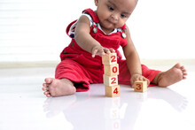 African Baby Girl In Red Cloth Sitting On Floor Playing With Wooden Blocks, Wooden Blocks With 2024 Number, Happy New Year