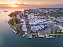 Aerial View Of Sunrise Over A City Waterfront On The The Side Of A River Flowing Out To The Ocean
