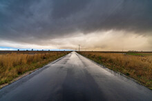 Wide Angled View Down A Country Road With Bright Gap Under Dark Storm Clouds