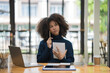 © Songsak C - Portrait of a pretty young black woman a serious working on a laptop sitting on the desk.