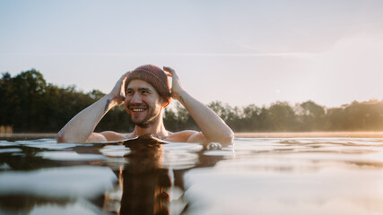 Young man soaks in the winter lake at morning. Male person taking care of his health