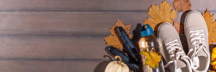 Autumn sport fitness background. Outdoors fall workouts concept. Running sneakers, dumbbell barbell discs, jump rope, water bottle, wooden background, with autumn leaves, pumpkins top view copy space