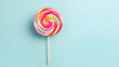Colorful lollipop swirl on stick, striped spiral multicolor candy on blue pastel background