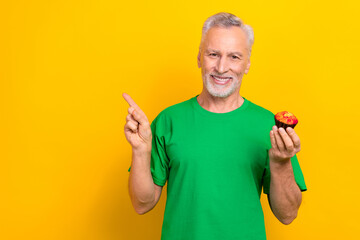 Photo of cool positive man wear green t-shirt enjoying muffin showing finger empty space isolated yellow color background