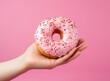 Female hand with pink donut on minimalist background