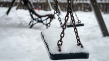 Closeup Of Snow Slowly Covering Empty Chain Swings On Winter Children Playground At Park
