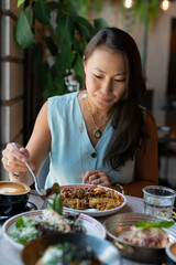 Wall Mural - A young Asian woman sits eating pasta at a table in a cafe.