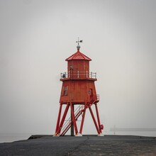 A Tall Red Lighthouse Tower Sitting On Top Of A Rocky Shore