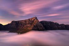 View Of Morning Fog Over Table Mountain With City Lights During A Dramatic Sunrise, Cape Town, South Africa.