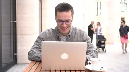 Wall Mural - Works online remotely sends an email. A happy man is a student. A young male programmer with glasses uses a laptop.