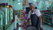 © Marco - One happy black senior employee standing at supermarket cashier smiling at camera wearing apron uniform. Charismatic friendly African American staff of Grocery store
