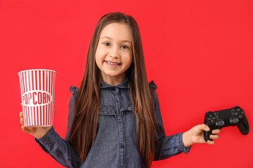 Wall Mural - Little girl with game pad and popcorn on red background