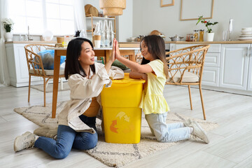 Wall Mural - Asian mother with her little daughter and recycle bin giving each other high-five in kitchen