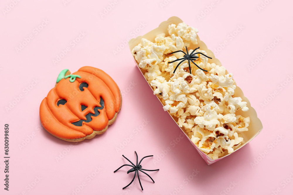 Paper box with tasty popcorn, cookie and spiders on pink background, closeup. Halloween celebration