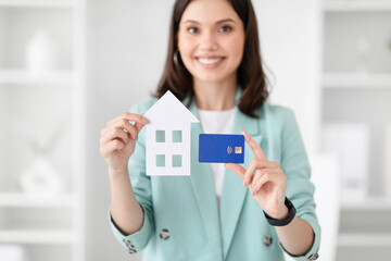 Wall Mural - Glad young caucasian businesswoman in suit hold credit card and house