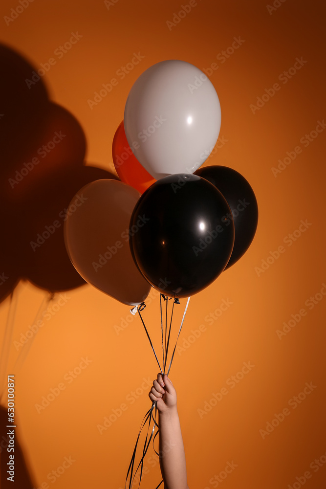 Female hand with Halloween balloons on orange background