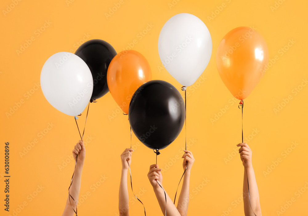 Female hands with different Halloween balloons on orange background
