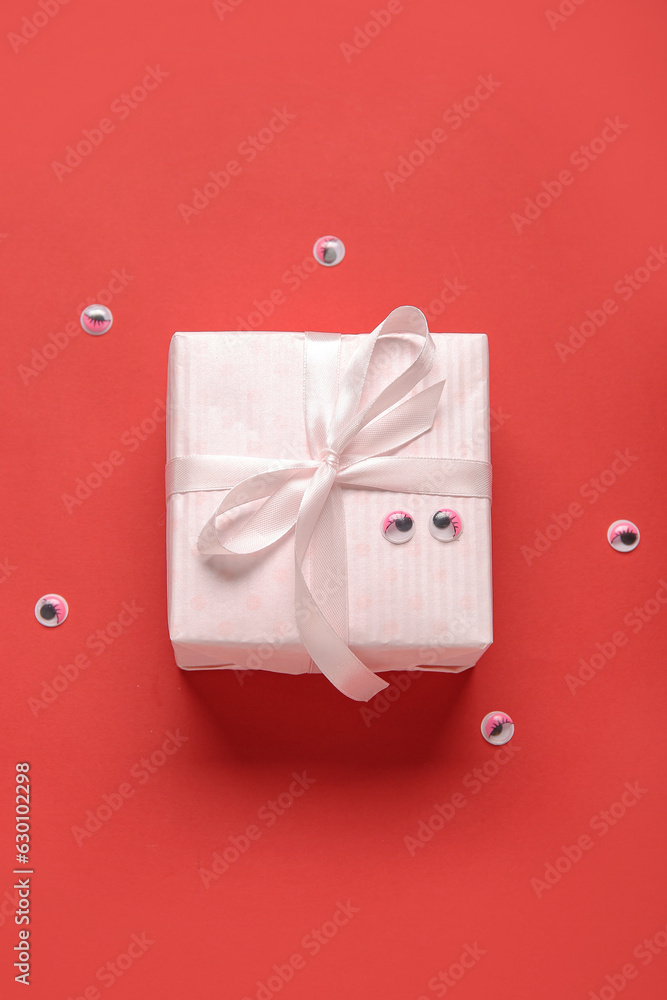 Composition with beautiful gift box and eyes for Halloween on red background