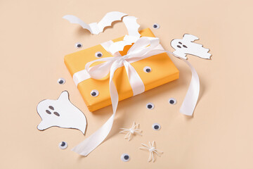 Composition with beautiful gift box and Halloween decor on beige background, closeup