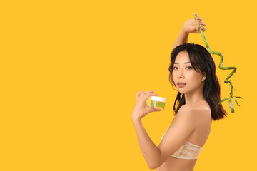 Sticker - Beautiful young Asian woman with scrub and bamboo on yellow background