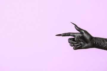 Black hand of witch pointing at something on purple background. Halloween celebration