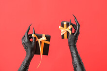 Black Hands Of Witch With Gift Boxes On Red Background. Halloween Celebration