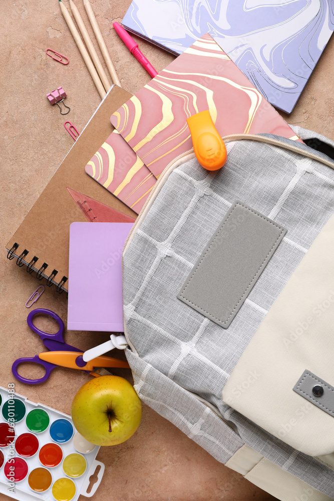Grey school backpack with notebooks, apple and watercolors on beige grunge background
