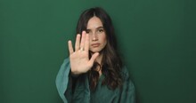 Brunette Woman Making Hands Stop Action Sign. I Said, No. Angry Frustrated Young Woman Showing Crossed Arms In X Gesture Sign And Looks On Camera. Forbidden Gesture Standing Isolated Green Background.