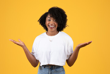 Happy surprised young black curly woman in white t-shirt spread arms to sides, hold empty space