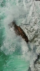 Wall Mural - Sea waves and stone rock from above. Turquoise water background top view. Vertical video 4k