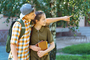 school students, a teenage boy and a girl are walking down the street, having fun, a boy pointing his finger, a bright summer day in a city park