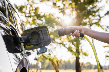 young woman plugging in the charger in a black electric car, renewable energy concept