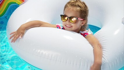 Poster - Little girl in sunglasses resting on white pool balloon